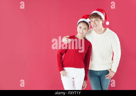 Young smiling couple wearing santa hats plaçant les mains sur les épaules avant de Banque D'Images