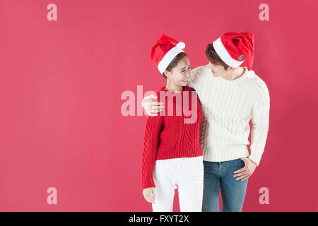 Jeune couple wearing santa hats in hans plaçant sur les épaules Banque D'Images