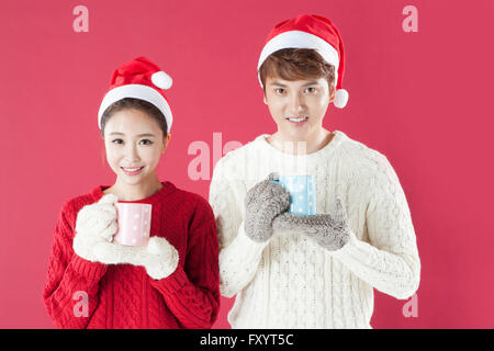 Portrait of young woman wearing santa hats et mitaines holding mugs regarder/ Banque D'Images