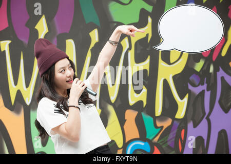 Side view portrait of young smiling woman in style hip-hop holding un microphone vers ro une bulle contre graffiti art Banque D'Images