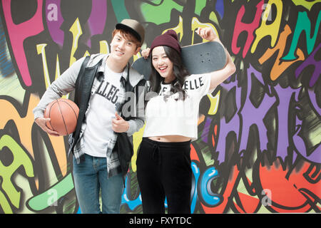 Young smiling couple dans un style hip-hop tenant une basket-ball et d'un skateboard contre graffiti art Banque D'Images
