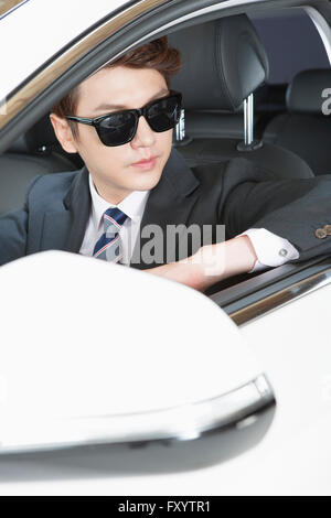 Portrait de jeune homme au début de la trentaine portant des lunettes de soleil et costume dans une voiture Banque D'Images