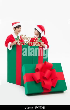 Smiling boy et gril à Santa's vêtements à présent fort avec décoration de Noël face à face Banque D'Images