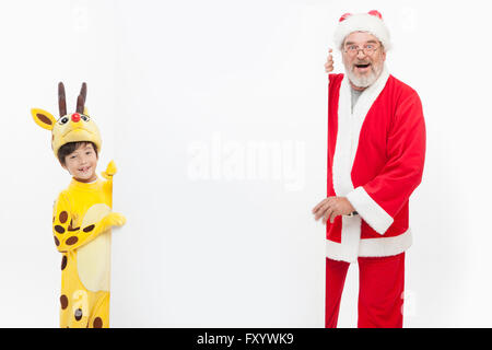 Smiling boy habillé comme un renne et souriant Santa avec un conseil fixant à l'avant Banque D'Images