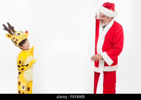 Smiling boy habillé comme le renne et souriant Santa avec un conseil face à face Banque D'Images