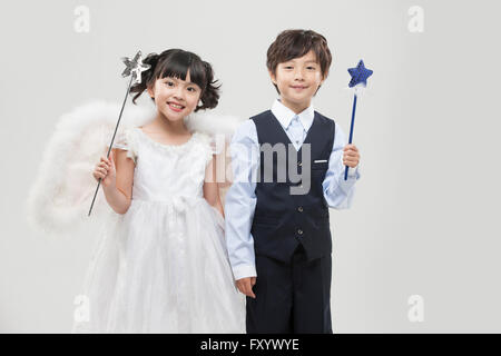 Smiling girl habillé comme angel et smiling boy in suit holding a chaque baguette avant fixant Banque D'Images
