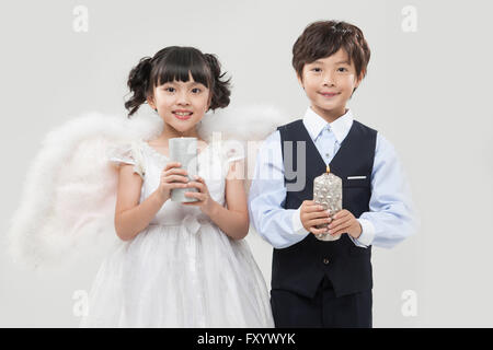 Portrait of smiling girl habillé comme angel et smiling boy in suit holding nouvelle chaque fixant à l'avant Banque D'Images