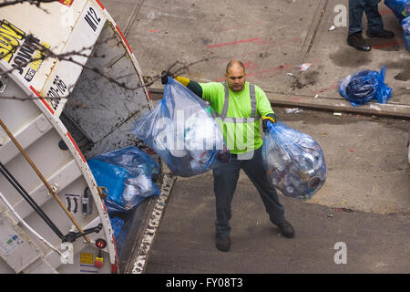 Un travailleur de l'assainissement dans la ville de New York de jeter des sacs poubelles de couleur bleue remplie de matières recyclables à l'arrière d'un camion à ordures Banque D'Images