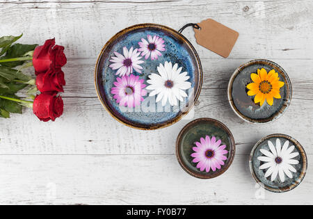 Roses rouges et gerbera flottant dans l'eau sur la table rustique en bois blanc avec gift tag. Vue de dessus avec l'exemplaire de l'espace. Banque D'Images