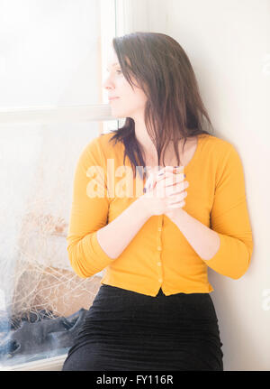 Femme assise par fenêtre, regardant ailleurs. Image Style de vie montrant une femme en attente et la pensée. Banque D'Images