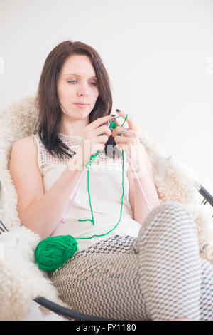 Tricot femme. Elle est assise sur une chaise dans votre intérieur. Image Style de vie montrant activité de loisirs et passe-temps. Banque D'Images