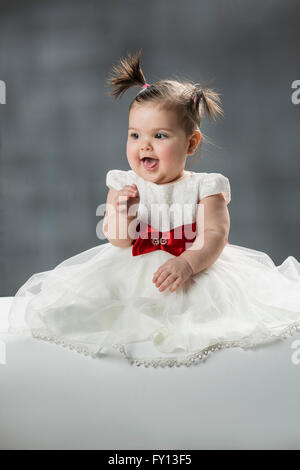 Cute baby girl avec bouche ouverte contre l'arrière-plan gris Banque D'Images