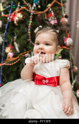 Cute baby girl sitting avec arbre de Noël en arrière-plan Banque D'Images