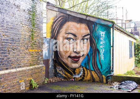 Graffiti murale représentant une fille asiatique sourire peint sur le mur d'un petit immeuble. Mur de brique sur le côté. Banque D'Images