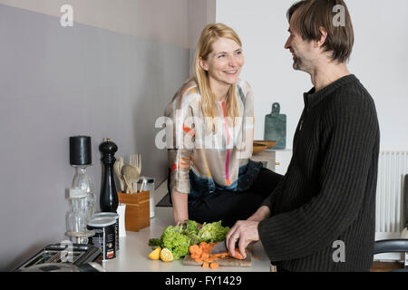 Smiling mature woman looking at man cutting vegetables in kitchen Banque D'Images