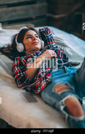 Trendy young woman listening music while lying on bed at home Banque D'Images