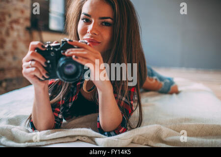 Portrait of young woman holding camera Nikon en position couchée sur le lit chez lui Banque D'Images