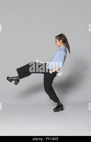 Jeune femme debout sur une jambe contre l'arrière-plan gris Banque D'Images