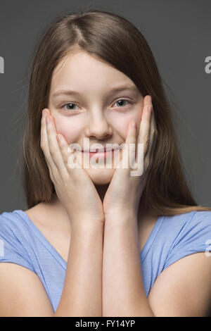 Close-up portrait of smiling girl with head in hands against gray background Banque D'Images