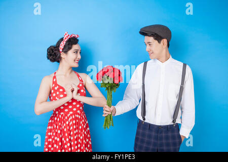 Young smiling man giving un bouquet de roses rouges à une jeune femme au style rétro Banque D'Images