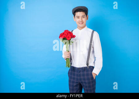 Jeune homme souriant style rétro en tenant un bouquet de roses rouges fixant à l'avant Banque D'Images