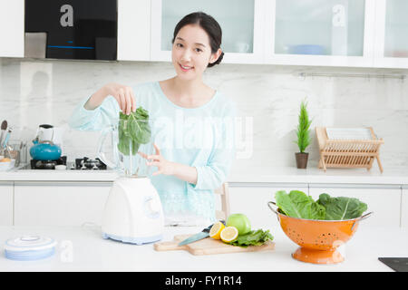 Jeune femme souriante de placer les légumes dans un blender dans la cuisine Banque D'Images