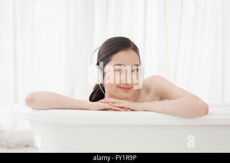 Portrait of young smiling woman listening to music dans une baignoire avant de Banque D'Images