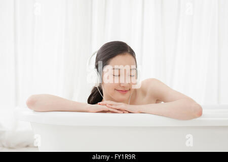 Portrait of young smiling woman listening to music fermer les yeux dans une baignoire Banque D'Images