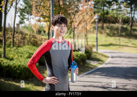 Portrait of young smiling man in sportswear holding water bottle at park Banque D'Images