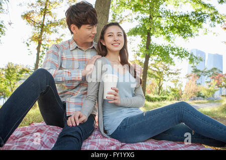 Couple assis sur l'herbe et une femme tenant une tasse de café Banque D'Images