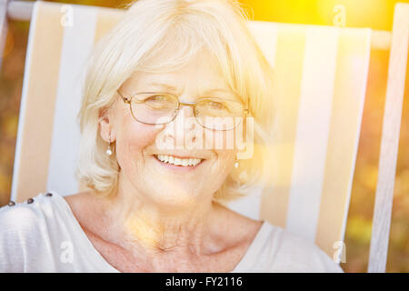 Happy senior woman wearing glasses et assis sur une chaise de terrasse en été Banque D'Images