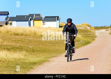 Skanor, Suède - 11 Avril 2016 : exercice cycliste le long d'une plage de sable fin par route ou chemin de randonnée avec une rangée de cabines d'être Banque D'Images