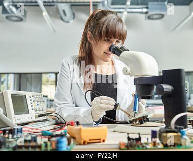 Technicien de sexe féminin, de 20 à 25 ans, avec une blouse blanche, une soudure du circuit dans un laboratoire électronique, Wattens Banque D'Images