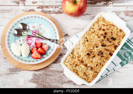 Crumble aux pommes dessert avec des fraises et crème à la vanille sur fond rustique en bois clair Banque D'Images