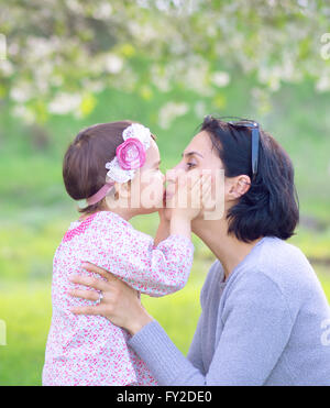 La famille, les enfants et les gens heureux concept - happy little girl hugging et embrasser sa mère sur fond vert Banque D'Images