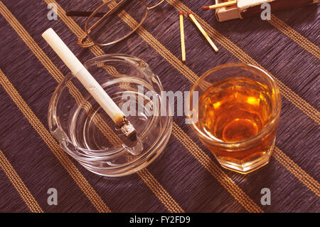 Verre de whisky et de cigarettes dans le cendrier. Banque D'Images