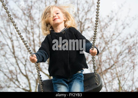 Petit enfant fille blonde s'amusant sur une balançoire à l'extérieur. Jeux d'été. Haut fille se balançant Banque D'Images