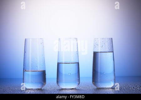 Un tiers pleine, à moitié rempli et deux tiers des verres à boire avec reflet dans les gouttes d'eau sur fond bleu et blanc Banque D'Images