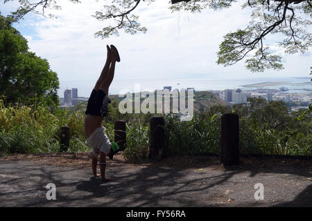 Un homme portant un chapeau, un t-shirt, short de basket-ball , et chaussons Handstands à Tantalus Mountain lookout point au-dessus de la ville de député Banque D'Images