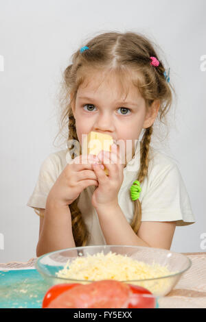 Fille de cinq ans avec des nattes manger du fromage à la table en face d'elle est une assiette de fromage râpé Banque D'Images