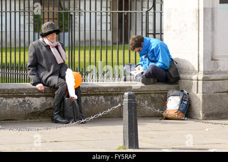 Femme âgée le repos s'est assis à côté de l'homme lecture le mur dans la ville universitaire de Cambridge, Cambridgeshire Angleterre Banque D'Images