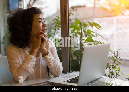 Young Asian Woman in headphones sitting in cafe avec ordinateur portable. Banque D'Images