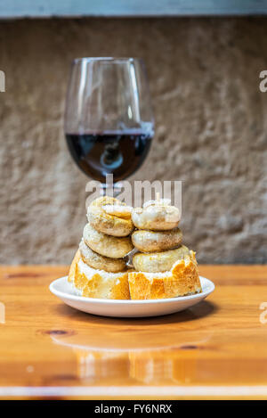 Les champignons typiques espagnoles pincho (Pintxo de champiñones) et une tasse de vin rouge en arrière-plan. Banque D'Images