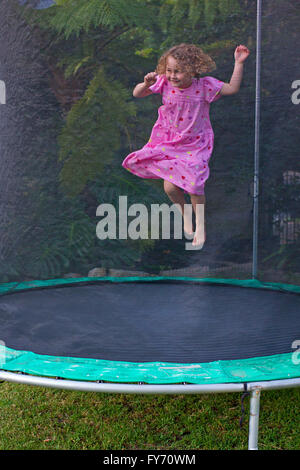 Jeune fille en robe rose de sauter sur le trampoline Banque D'Images