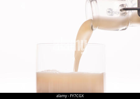 Le lait d'avoine est versé à partir de la bouteille dans un verre à boire, Close up. Arrière-plan blanc. Banque D'Images