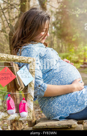 Belle femme enceinte extérieure de la pensée dans le parc sur un banc. Banque D'Images