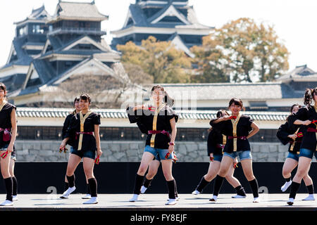 Japanese female dance troupe d'adolescentes, holding naruko, danser sur scène en plein air avec Château Kumamoto derrière eux, au cours de la fête de Yosakoi. Banque D'Images