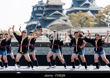 Japanese female dance troupe d'adolescentes, holding naruko, danser sur scène en plein air avec Château Kumamoto derrière eux, au cours de la fête de Yosakoi. Banque D'Images