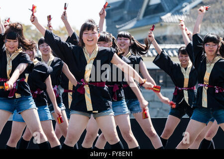 Japanese female dance troupe d'adolescentes, holding naruko, danser sur scène en plein air avec Château Kumamoto derrière eux, au cours de la fête de Yosakoi. Banque D'Images