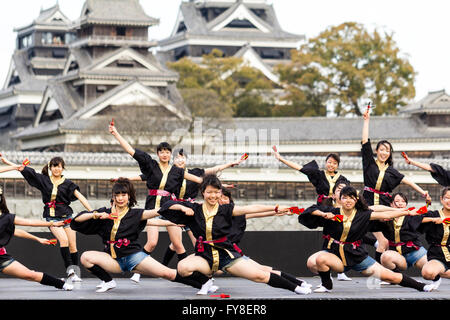 Japanese female dance troupe d'adolescentes, holding naruko, danser sur scène en plein air avec Château Kumamoto derrière eux, au cours de la fête de Yosakoi. Banque D'Images